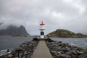 View over rocky Reine Breakwater leading to a small red and white lighthouse near Reine, Norway in...