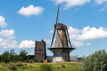 Fortified walls of historic town Woudrichem, the Netherlands with flour mill and characteristic square tower of Sint Martinus church against a white clouded blue sky