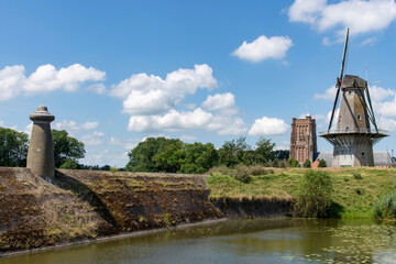 Fortified walls of historic town Woudrichem, the Netherlands with flour mill and characteristic square tower of Sint Martinus church against a white clouded blue sky