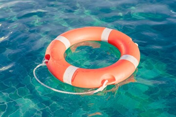 Bright orange life buoy floating in clear water during sunny weather