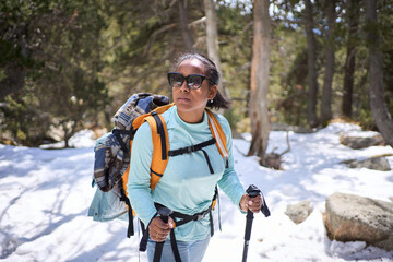 Female hiker enjoying a snowy mountain forest trail, equipped with backpack and trekking poles, embracing the serene winter landscape