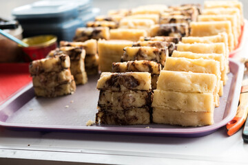 Sliced kue pukis (Indonesian mini pancakes) with chocolate and plain flavors, neatly arranged on a pink tray at a street food stall. Kue pukis is a traditional Indonesian snack made from flour, eggs, 