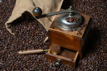 Rustic coffee grinder with a measuring spoon stand with a bag of coffee on a background of coffee beans