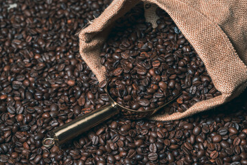 Jute sack full of coffee with a golden coffee scoop on a background of coffee beans