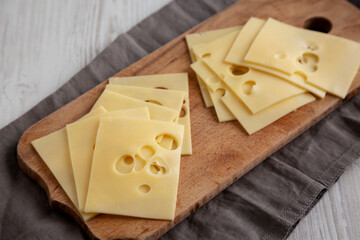 Slices of Maasdam cheese on a wooden board, side view.