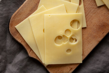 Slices of Maasdam cheese on a wooden board, top view. Close-up.