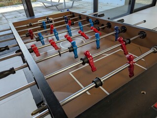 A top down view of a foosball table in a bar or café, all the minature plastic soccer or football players are visible and the handles to. they are ready to be played with.