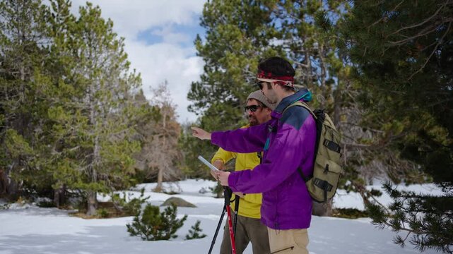 Two male hiker using digital map on mobile phone enjoying a snowy mountain forest trail. Only men equipped with backpack and trekking poles, embracing the serene winter landscape. Friendship and