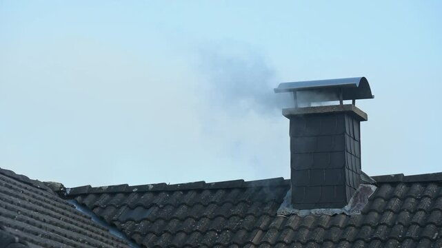 Smoke rising from a chimney on a roof of a residential house, blue sky background