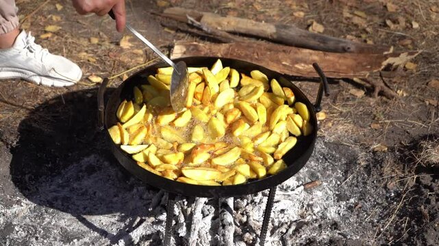 Cooking food on a campfire while hiking. Fried potatoes. Frying pan on a fire outdoors. Camp food in nature. Stir vegetables