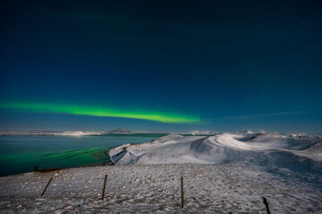 Aurora Borealis or Northern lights the amazing wonder of nature in the dramatic skies of Iceland. Night landscape with the green light and the white snow of winter