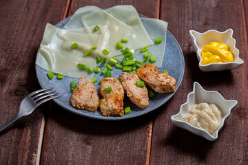 Thin khinkal with meat and greens, onions and different sauces in a plate
