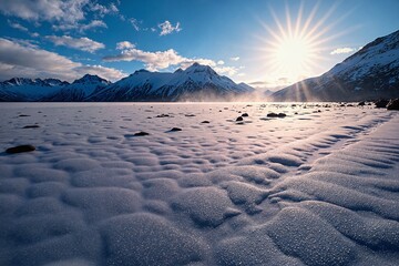  A serene winter landscape featuring snow-covered mountains rocks scattered across the ground and a vast expanse of frozen water stretching out 