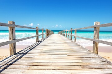 Obraz premium Wooden boardwalk leading to the turquoise ocean under a bright blue sky.