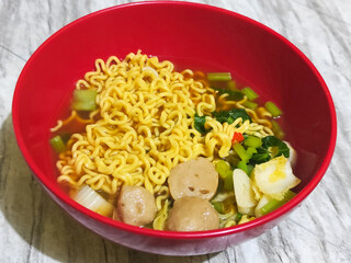 A bowl of Indonesian noodle soup with vegetables and meatball pieces.