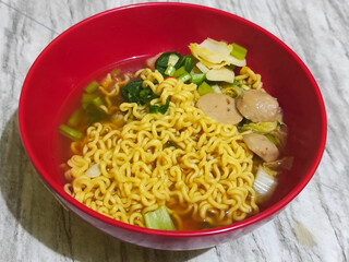 A bowl of Indonesian noodle soup with vegetables and meatball pieces.