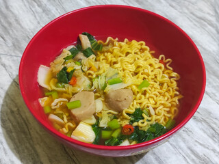 A bowl of Indonesian noodle soup with vegetables and meatball pieces.
