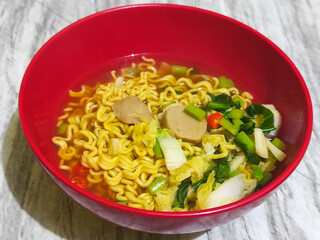 A bowl of Indonesian noodle soup with vegetables and meatball pieces.