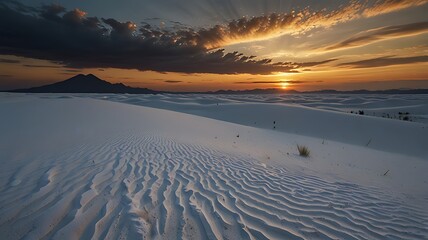 A stunning sunset over white sand dunes, with dramatic clouds and distant mountains.