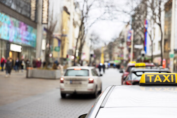 Taxi sign in focus on a urban street with pedestrians and vehicles in a city center