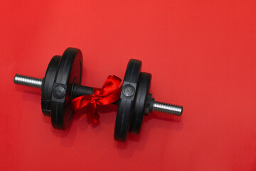 dumbbell for sports tied with a red satin ribbon, on a red background