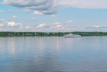 A small white motor ship is sailing along a wide river. An old pleasure boat. People are relaxing on the river. Entertainment for people related to sailing on a motor ship. River transport.
