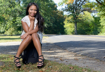 Sexy black woman staring along country road with bag waiting for ride - wearing short sundress