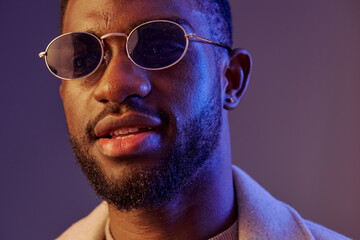 Obraz premium Portrait of a stylish young Black man wearing sunglasses, expressing confidence against a colorful background, ideal for fashion or lifestyle concepts