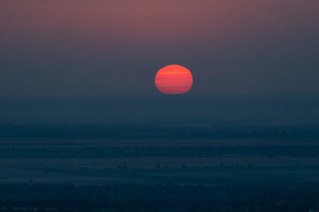 A striped red sunset sun over a dark city against a blue sky background. Horizontal photo.