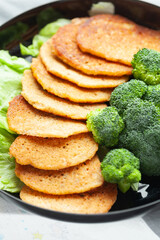 Golden-brown pancakes served with fresh broccoli florets on a black plate. A healthy and delicious meal.
