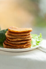 A stack of golden-brown pancakes sits on a white plate, accompanied by a side of fresh green vegetables. A simple, healthy, and delicious breakfast or snack.