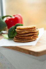 A stack of golden-brown pancakes sits on a wooden board, accompanied by fresh broccoli and a red bell pepper.  Healthy and delicious!