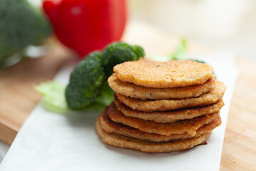 A stack of savory pancakes, golden brown and delicious, sits on a white surface near fresh broccoli and a red pepper.