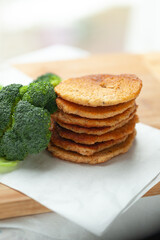 A stack of golden-brown pancakes sits next to a bunch of fresh broccoli on a wooden surface.  Healthy and delicious breakfast or snack.