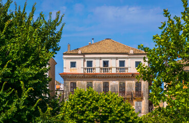 Old abandoned Venetian building peaking trough vibrant green trees in Corfu town, Greece