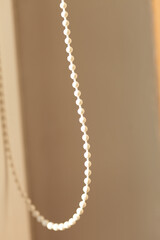 Close-up of a white beaded chain hanging against a muted beige background. The soft light...