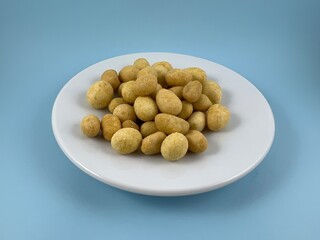 a plate of savory peanuts coated in flour and egg isolated on blue background