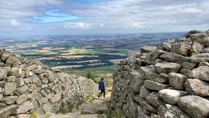 A female hiker walks down the stone steps of the ancient hill fort on top of Mither Tap in the Bennachie Mountain Range - Nr Inverurie, Aberdeenshire, Scotland, UK