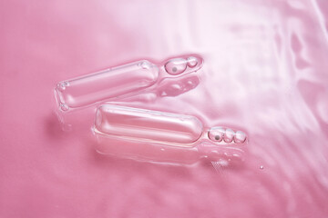 Ampoules in water on a pink background.