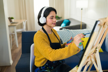 Artist painting vibrant canvas, wearing headphones, immersed in creative process within sunlit home...