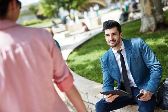 Handsome young businessman sitting at park flirting with woman passing by.
