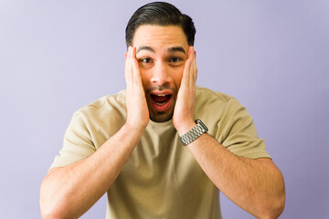Shocked hispanic man holding face in disbelief on purple background