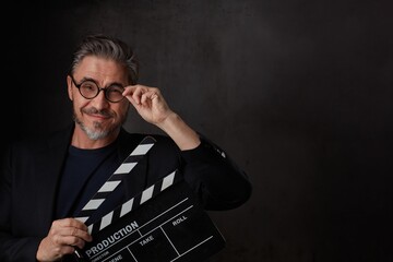 Happy movie director holding black clapper board. Movie director starting film. Copy space, dark background.