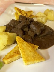 Delicious beef stew with potatoes and grilled polenta on a white plate