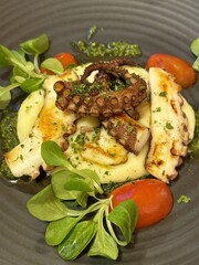 Grilled octopus on creamy mashed potatoes with greens and tomatoes