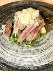 Sliced steak on arugula with shredded parmesan cheese on black plate