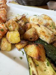 Grilled seafood and roasted potatoes with zucchini on white plate garnished with parsley