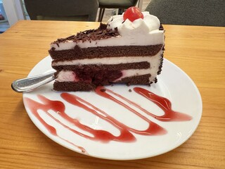 Delicious black forest cake slice with cherry topping on white plate