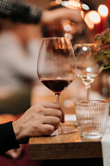 A hand holding a glass of red wine on a wooden table during an elegant dinner gathering