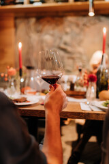 Hand holding a glass of red wine at a cozy dinner gathering with candles and elegant table decor